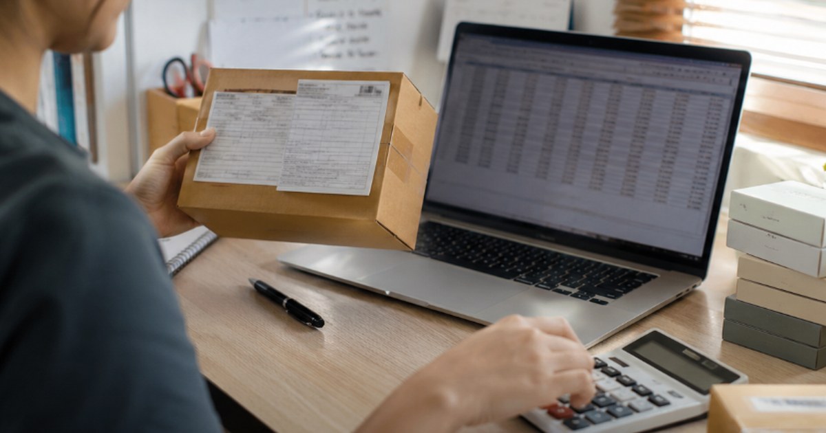 A reseller using a landed cost calculator spreadsheet while weighing a package for a customs shipment